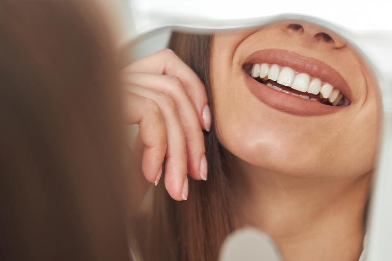 A woman with a smile looking at her reflection in a mirror.