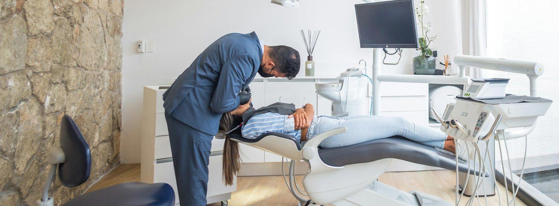 The image shows a modern dental clinic interior with various pieces of equipment, including a dental chair and an X-ray machine.